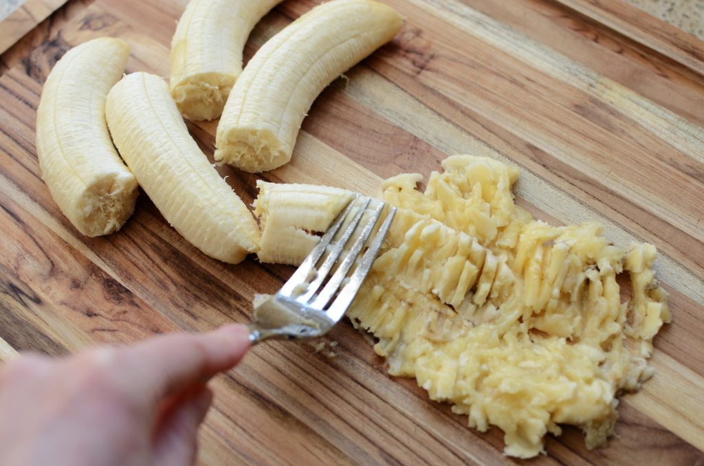 Mashed banana with fork on wooden cutting board