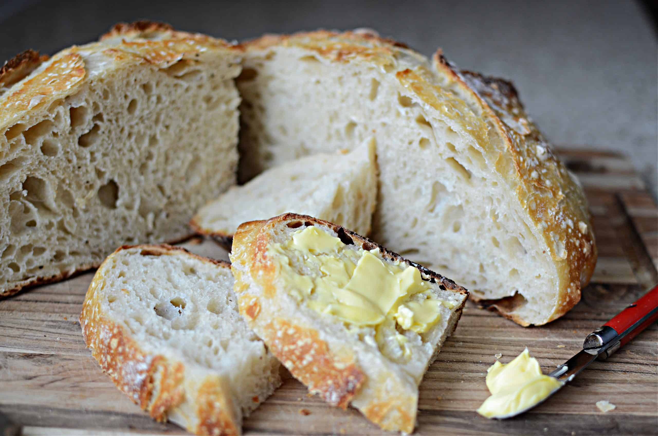 Sourdough bread loaf sliced and cut pieces with butter and butter knife on wooden cutting board