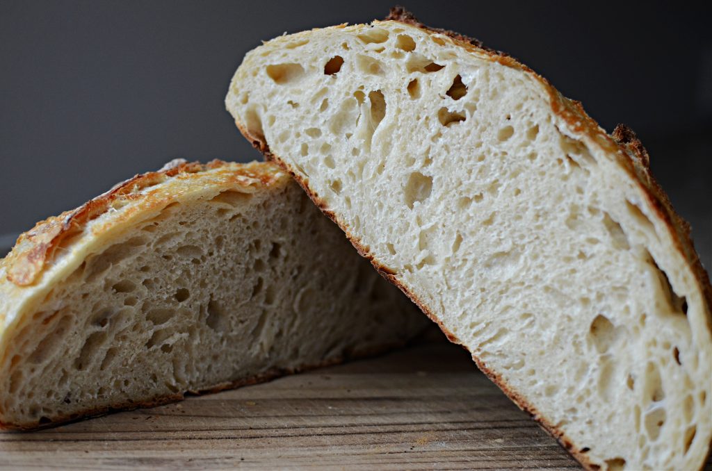 Two halves of a sourdough bread loaf stacked on top of one another on wooden cutting board.