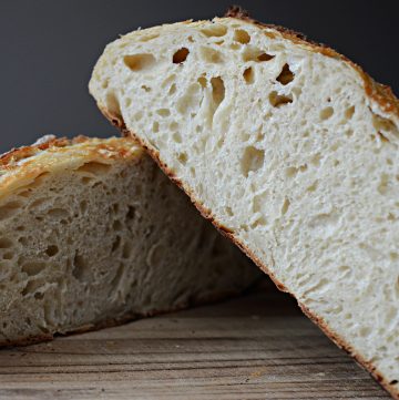 Two halves of a sourdough bread loaf stacked on top of one another on wooden cutting board.