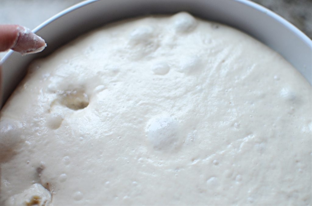 Sourdough bread dough in white bowl poked with floured finger