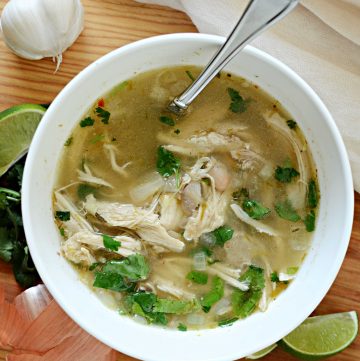 White chicken chili in white bowl with spoon on wooden cutting board