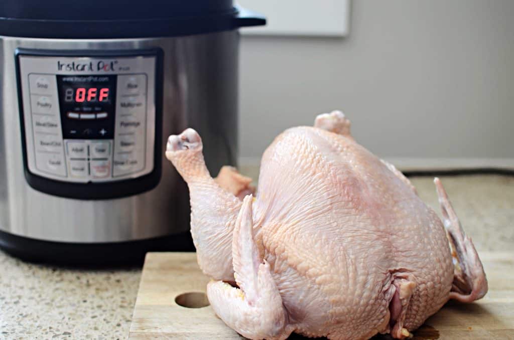 Whole raw chicken on cutting board with Instant Pot in background
