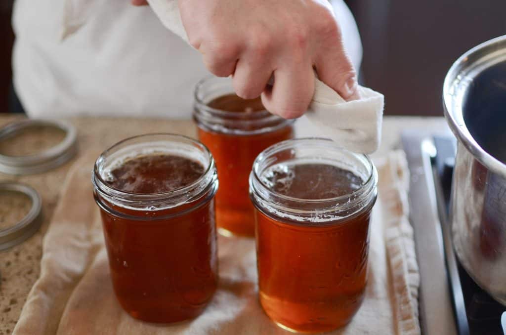 Wiping mouth of jar filled with maple syrup with white cloth