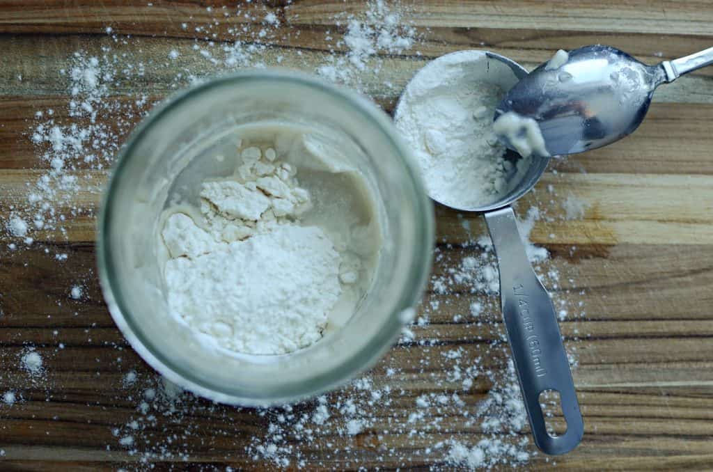 sourdough starter, flour in measuring cup and spoon on wood cutting board