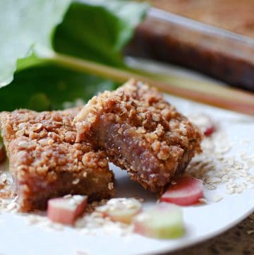 Two rhubarb bars on white plate with oatmeal and sliced rhubarb