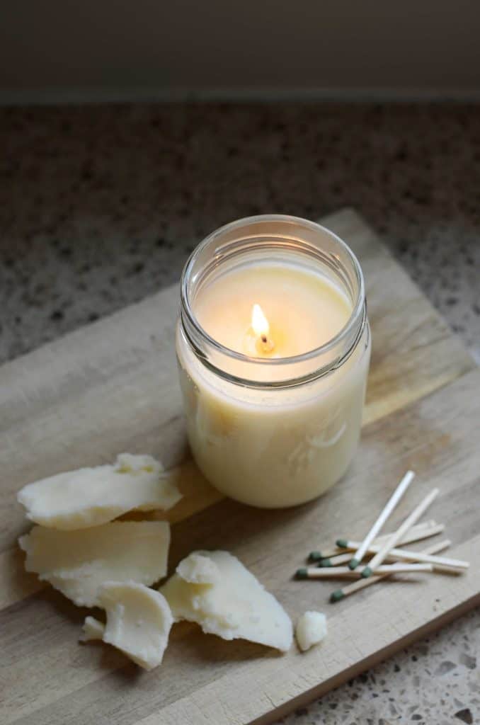 Lit tallow candle in mason jar on wood cutting board with matches and chunks of tallow.