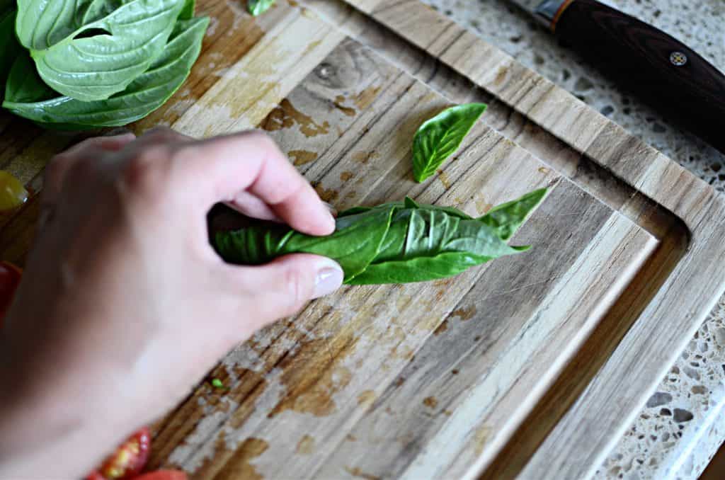 Rolled basil leaves on wood cutting board