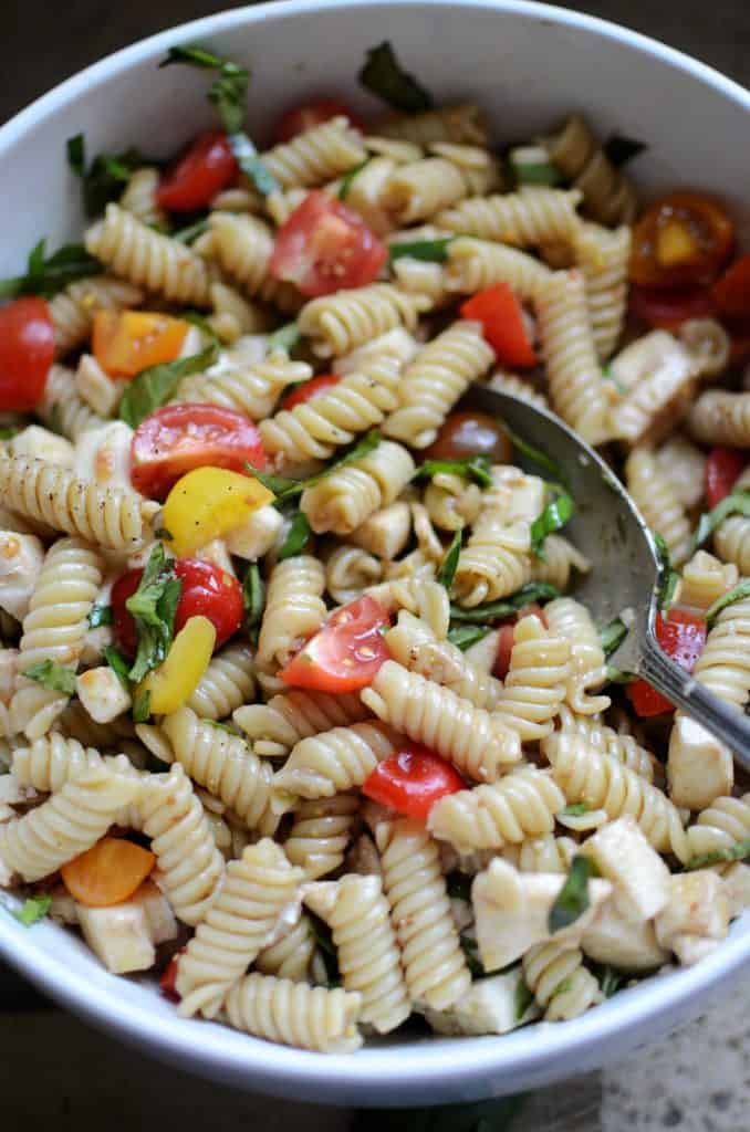 Pasta salad in white bowl with serving spoon.