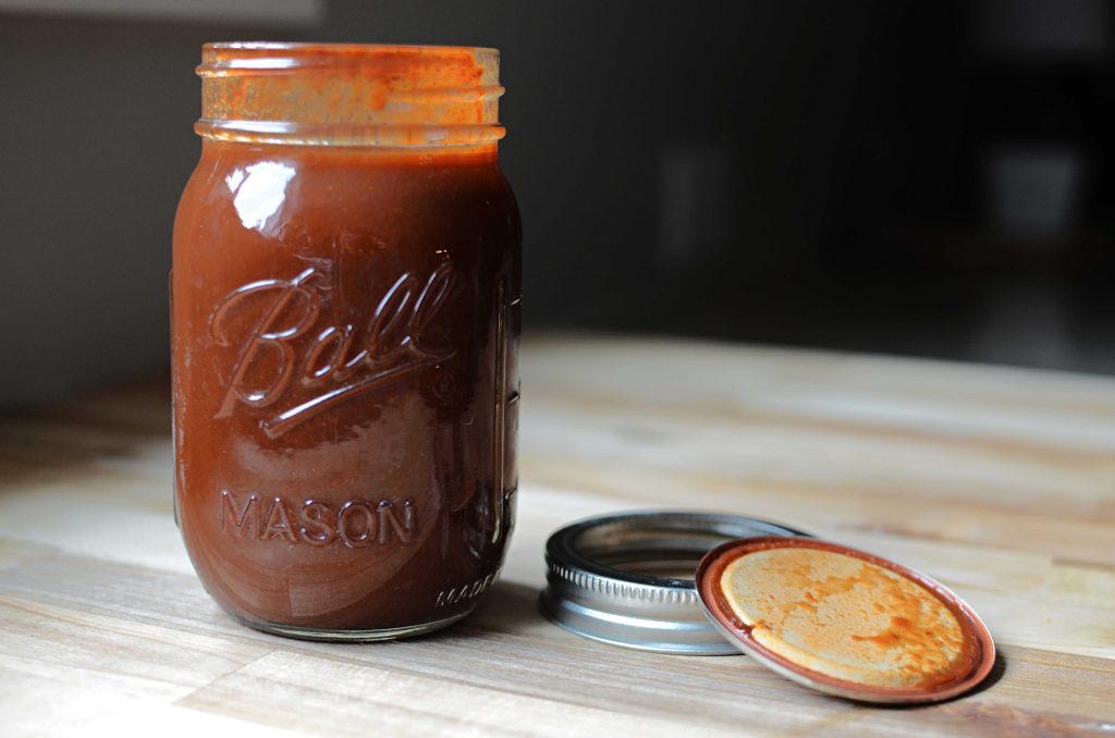 Ball mason jar of enchilada sauce with lid and band next to it.