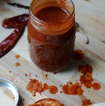 Enchilada sauce in jar with dried chilies and spoon.