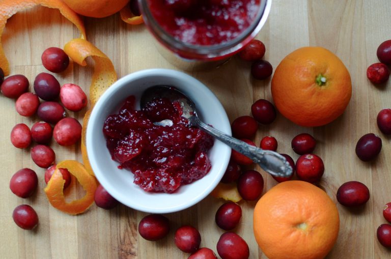 Cranberry sauce in white dish with spoon, surrounded with cranberries and orange