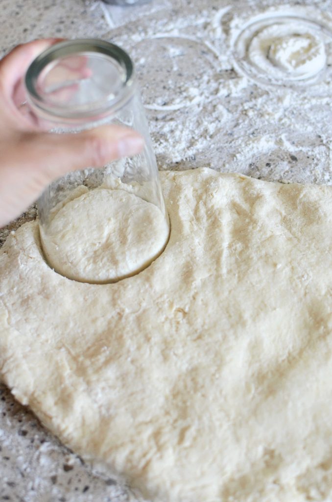 Using drinking glass to cut circles out of homemade biscuit dough made from scratch