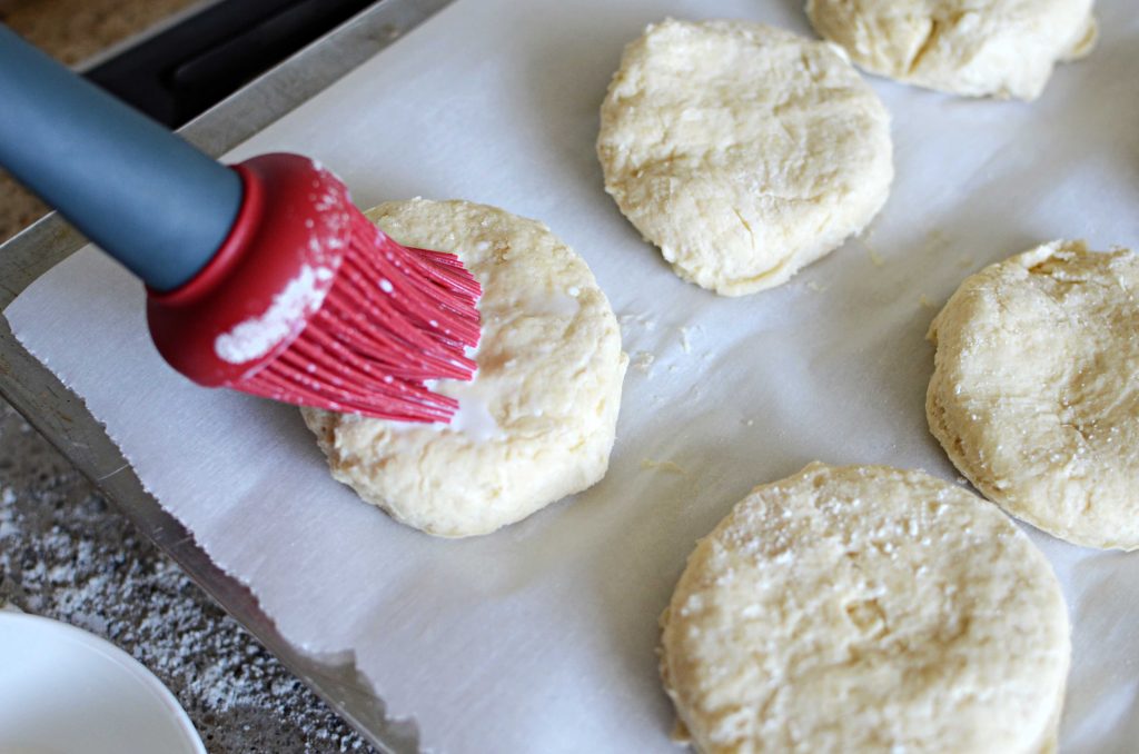 brushing milk on cut out biscuits, which is on parchment paper.