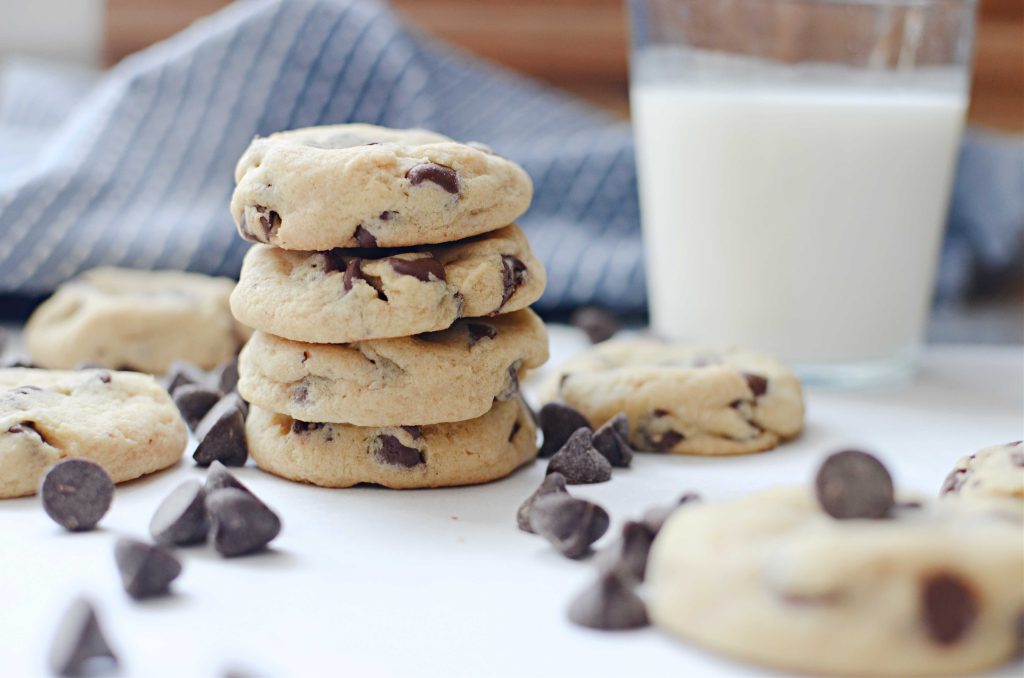 Stacked soft batch chocolate chip cookies with chocolate chips and a glass of milk