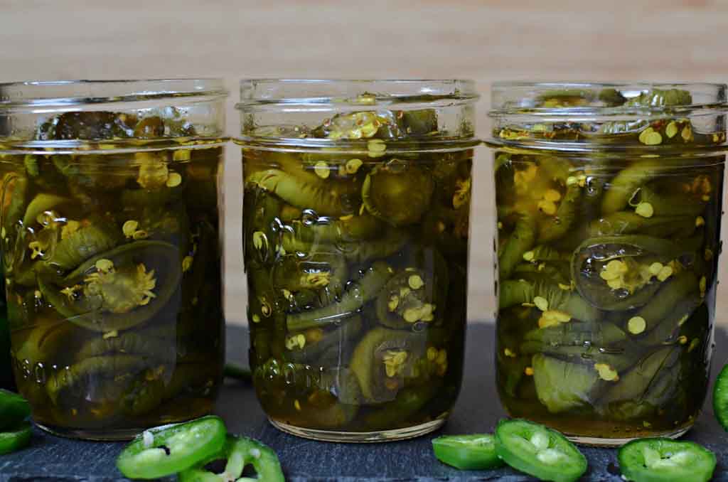 mason jars of candied jalapenos with out lids and jalapeno slices scattered around