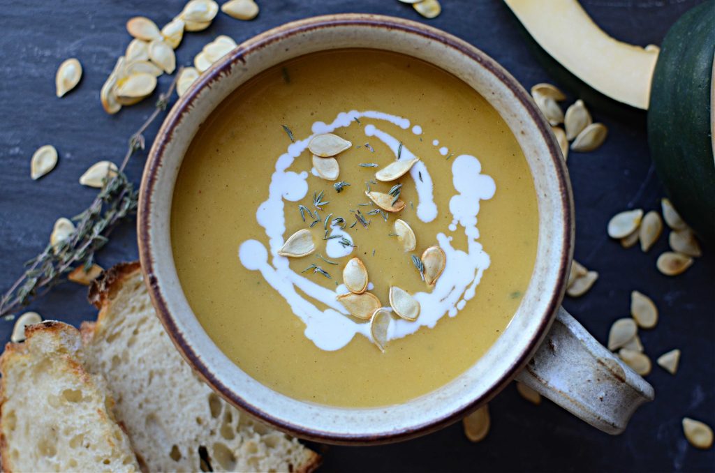 Creamy acorn squash soup in bowl with drizzle of coconut milk and roasted seeds