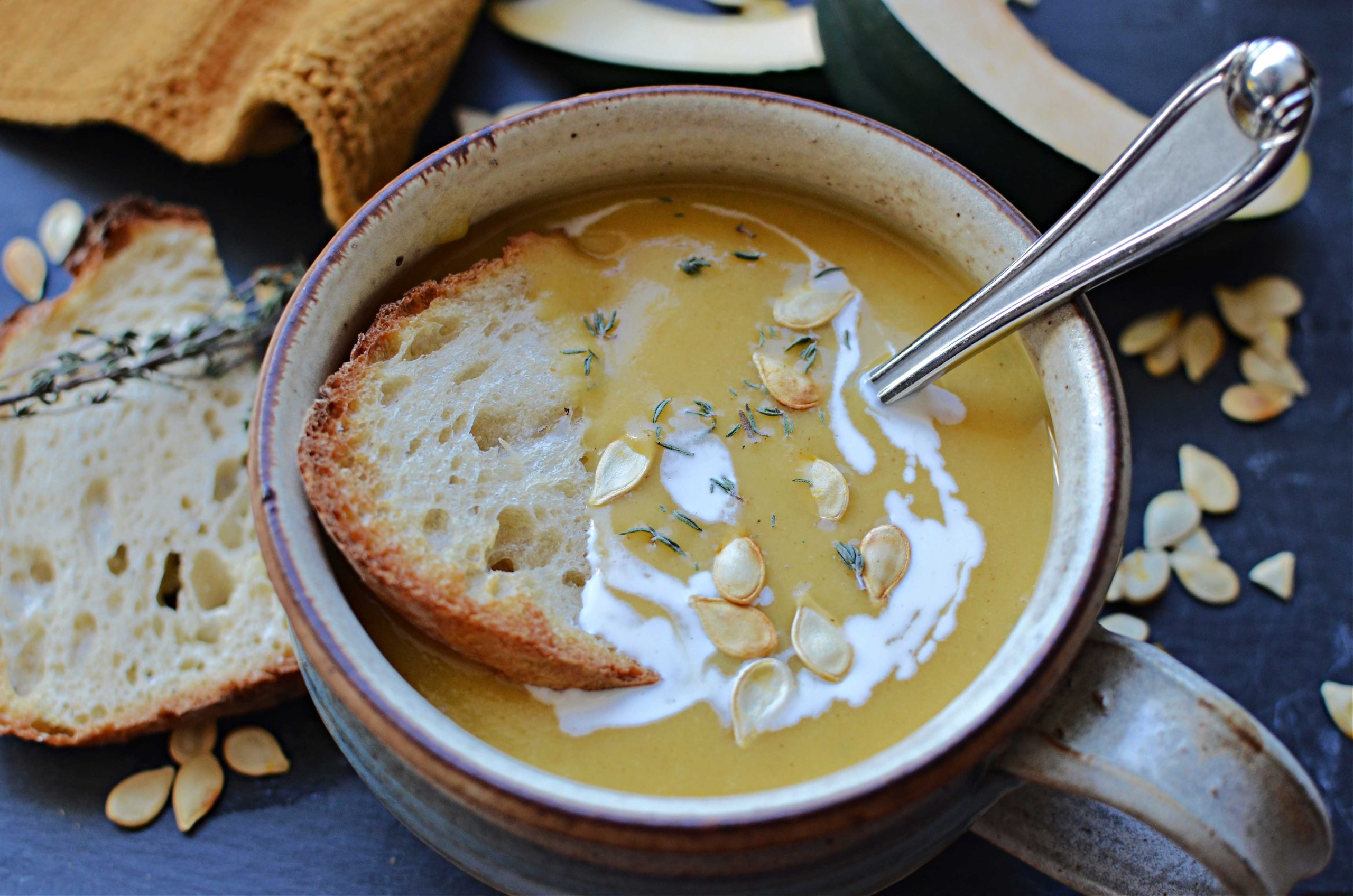 Acorn squash soup in bowl with spoon, coconut milk drizzle, roasted squash seeds and bread