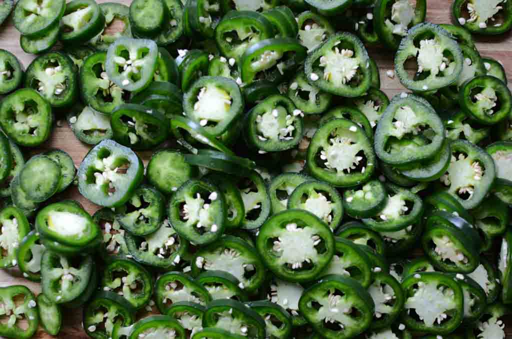 A wooden cutting board full of sliced jalapenos