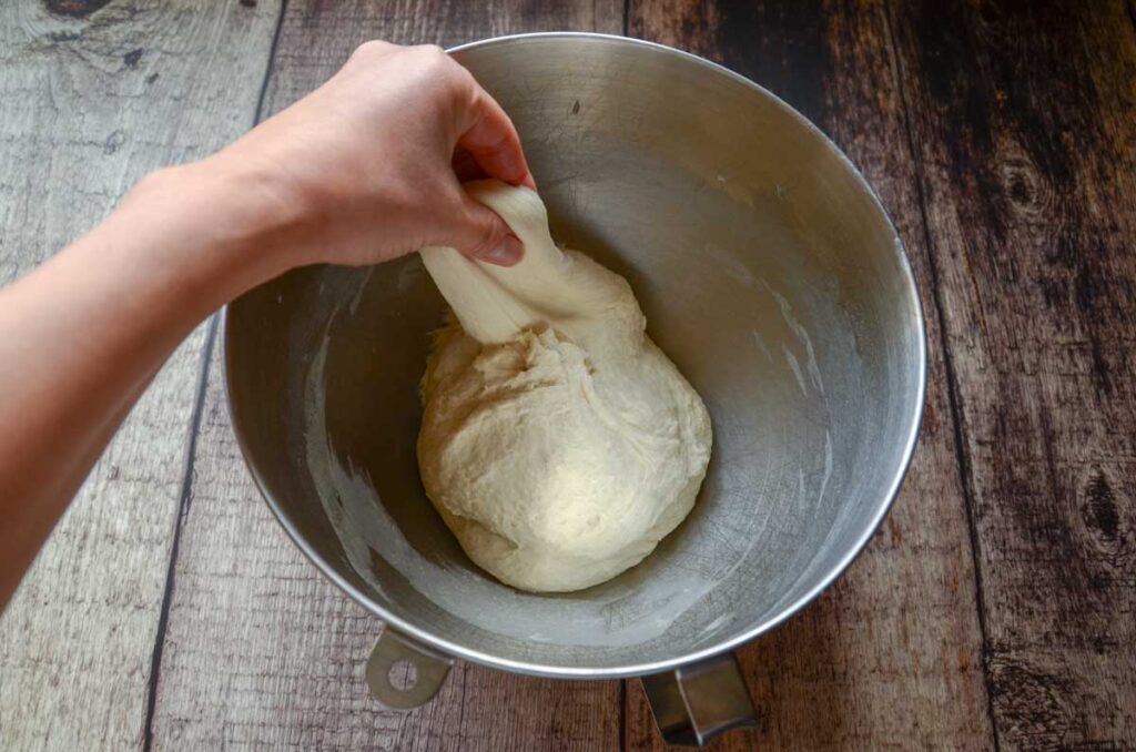 stretching sourdough English muffin dough in a metal bowl 