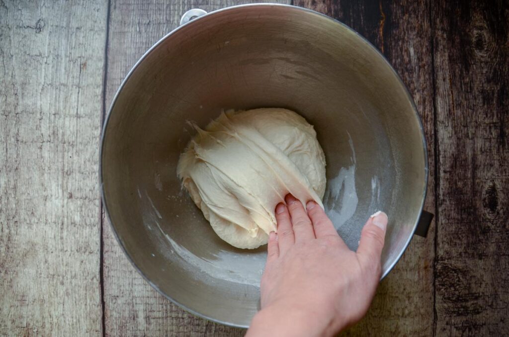 folding sourdough English muffin dough in a metal bowl 