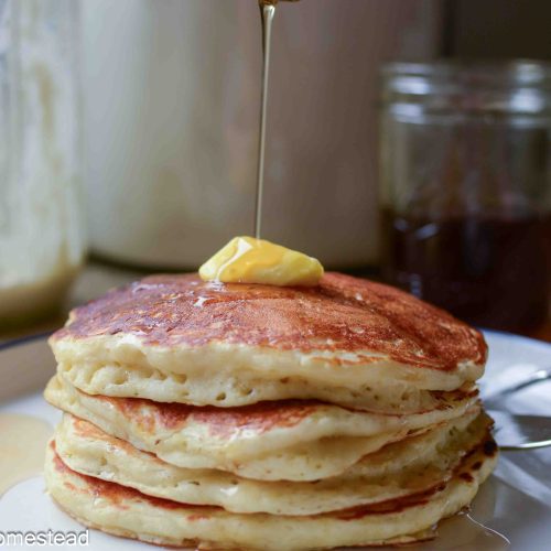 A stack of pancakes with a pat of butter and maple syrup being poured over