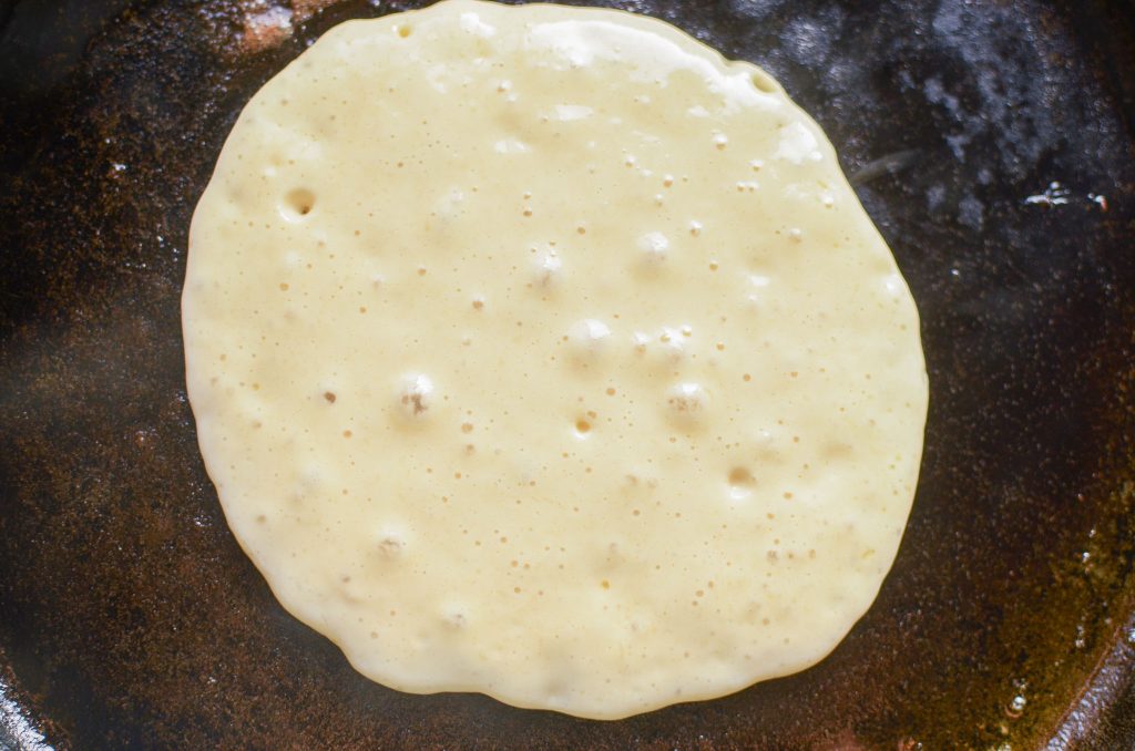 Sourdough pancake batter on first side on cast iron skillet, and pancake on second side.  