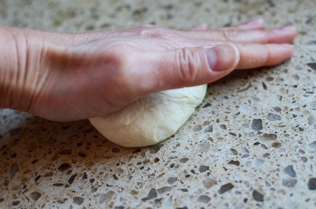 Using the palm of your hand rolling the sourdough tortilla dough into a ball