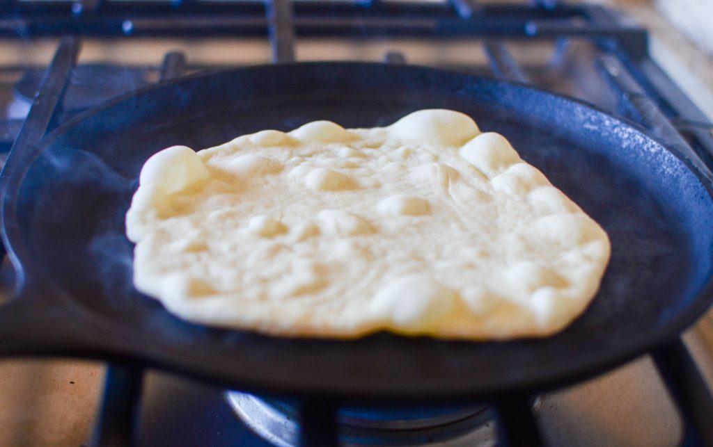 Sourdough flour tortilla on a hot cast iron skillet with bubbles