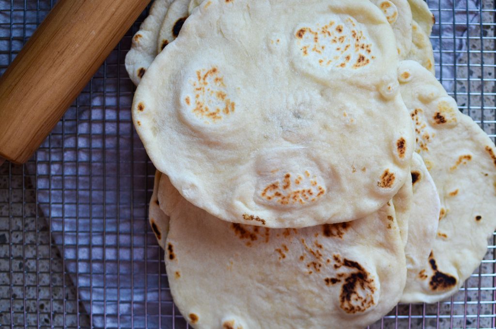 Sourdough flour tortillas stacked on wire rack.