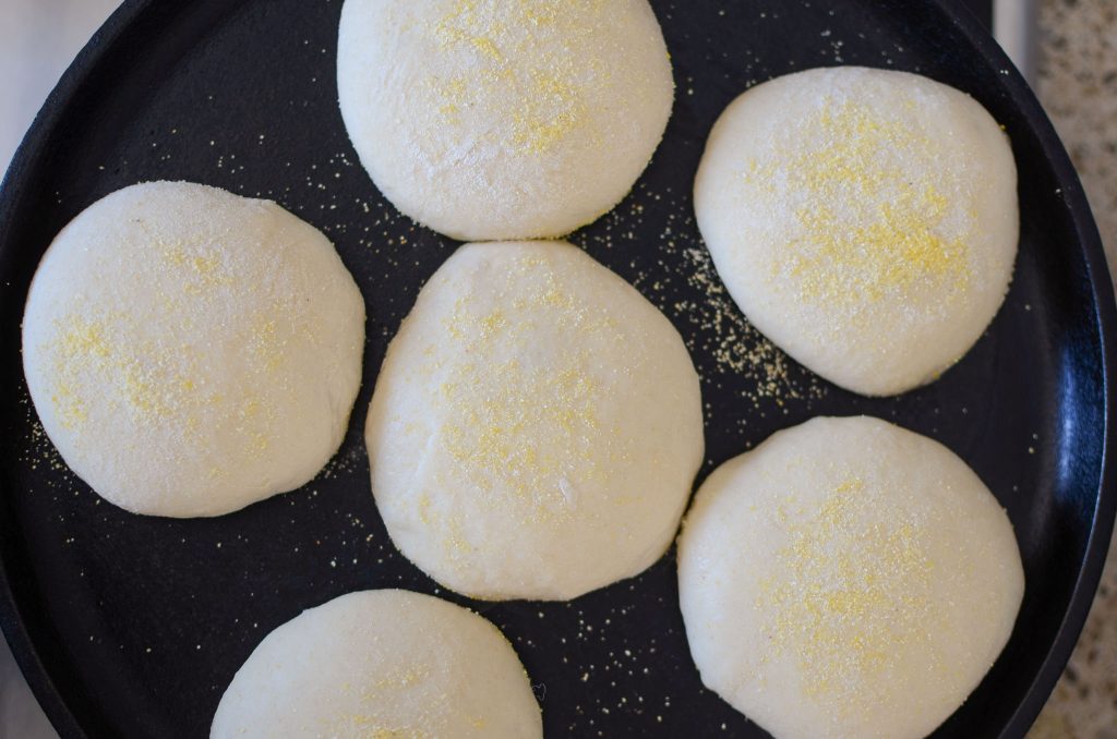 Cooking 1st side of sourdough English muffins on cast iron pan viewed from overhead.