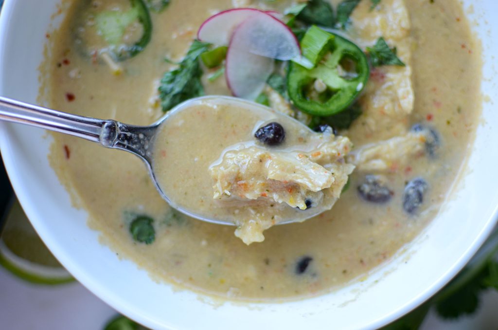 A spoonful of creamy chicken poblano pepper soup above a bowl of soup