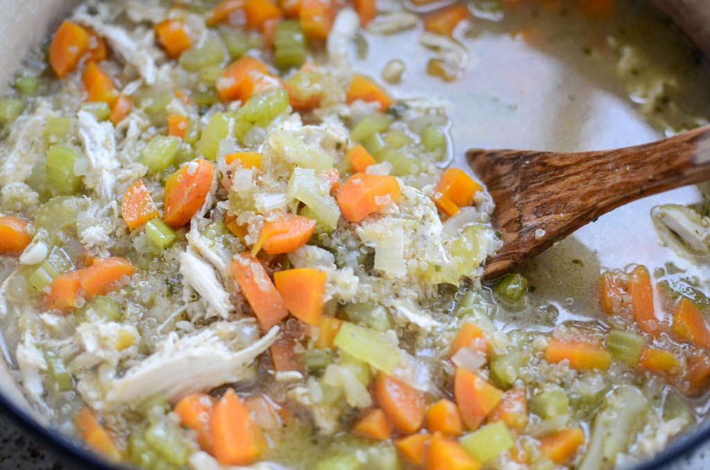 Chicken quinoa soup in large pot with wooden spoon.