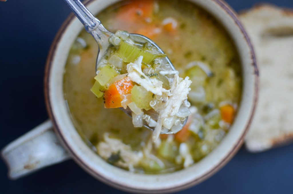 a spoonful of chicken quinoa soup lifted above a cup of soup