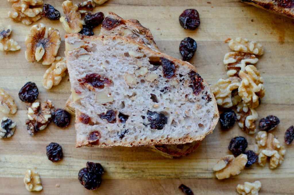 stacked slices of cranberry walnut bread with walnuts and dried cranberries scattered around bread