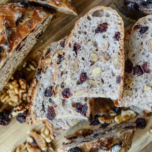 Slices of cranberry walnut bread stacked with dried cranberries and walnuts scattered around