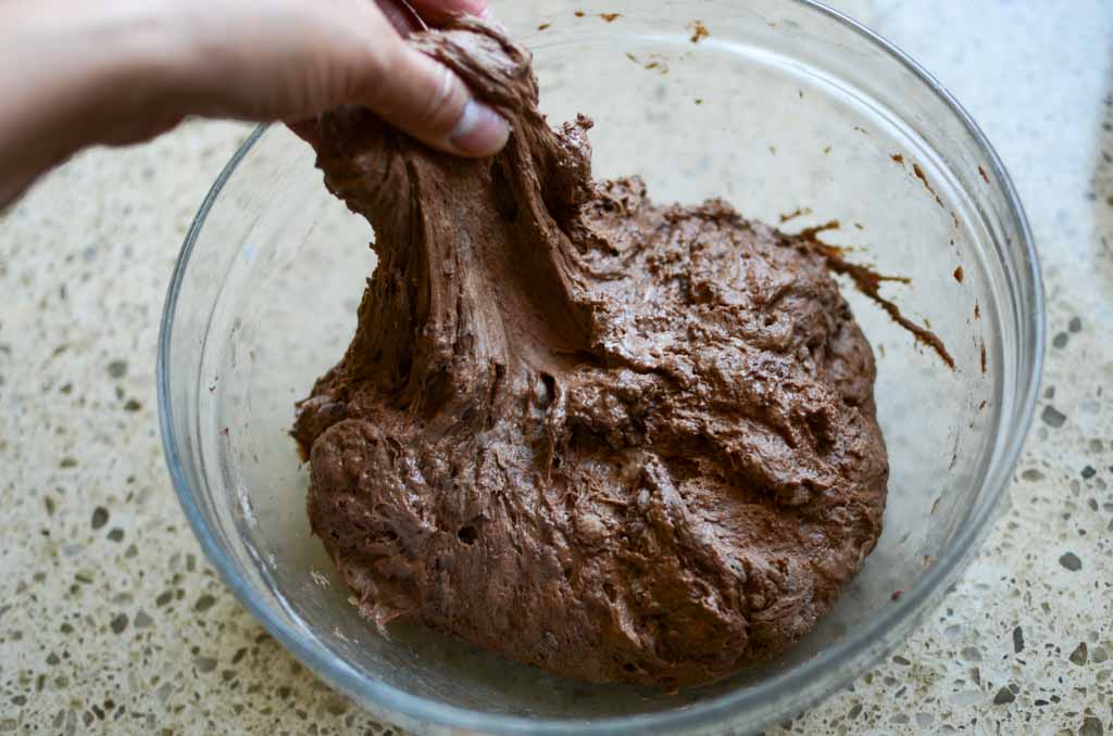 grabbing the side of sourdough chocolate bread dough in glass bowl