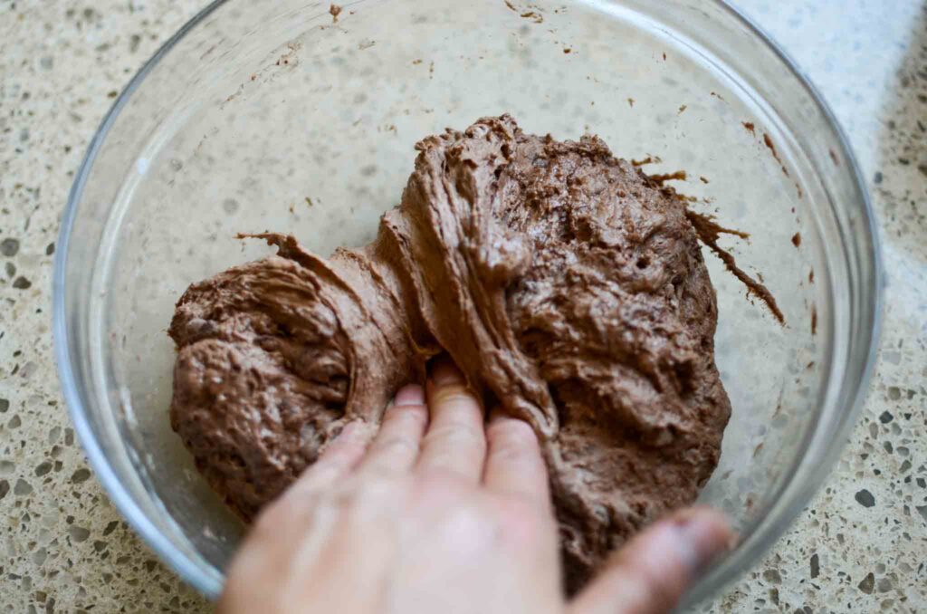 folding sourdough chocolate bread dough in glass bowl