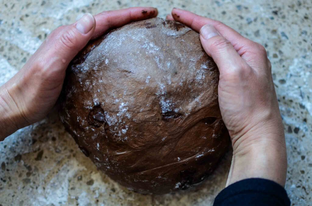 Using two hands to shape a loaf of double chocolate sourdough dough