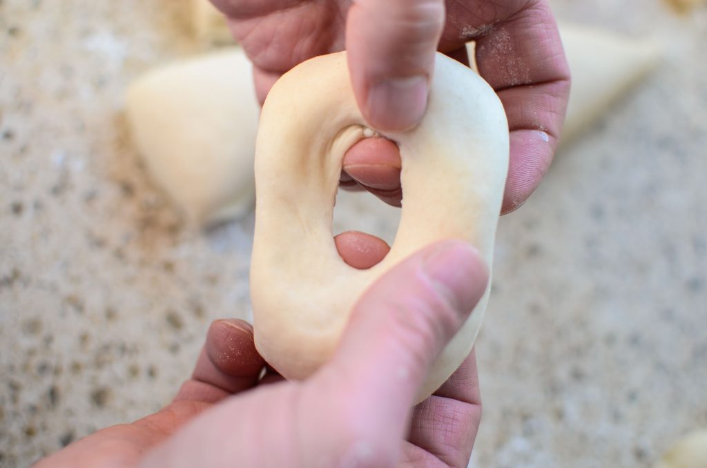 two hands poking a hole in the sourdough bagel dough ball and stretching out