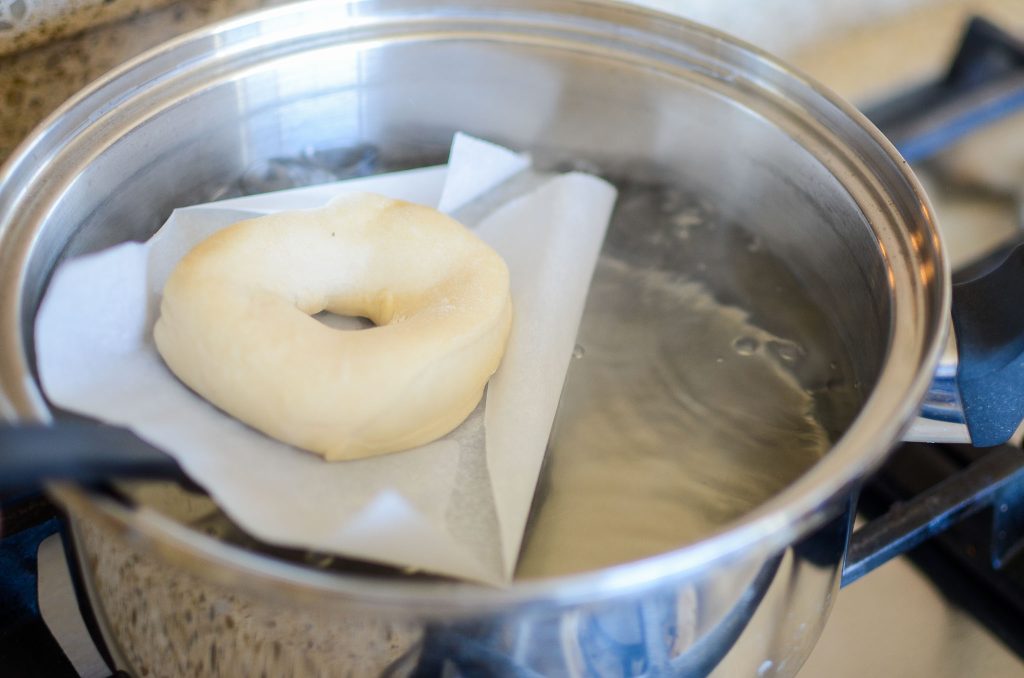 dropping a sourdough bagel on parchment paper into boiling water