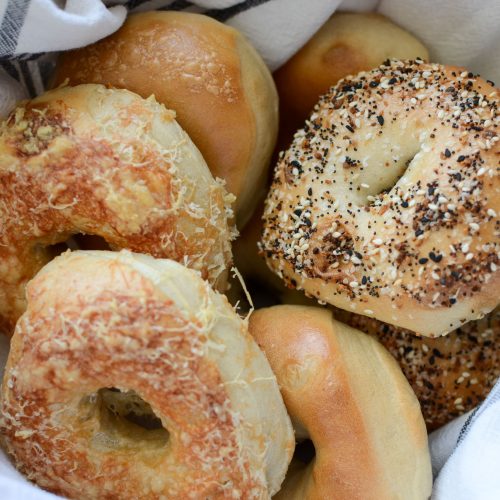 Linen-lined basket full of sourdough bagels with various toppings