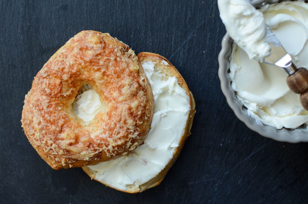 Cheese sourdough bagel with cream cheese and dish of cream cheese and spreading knife