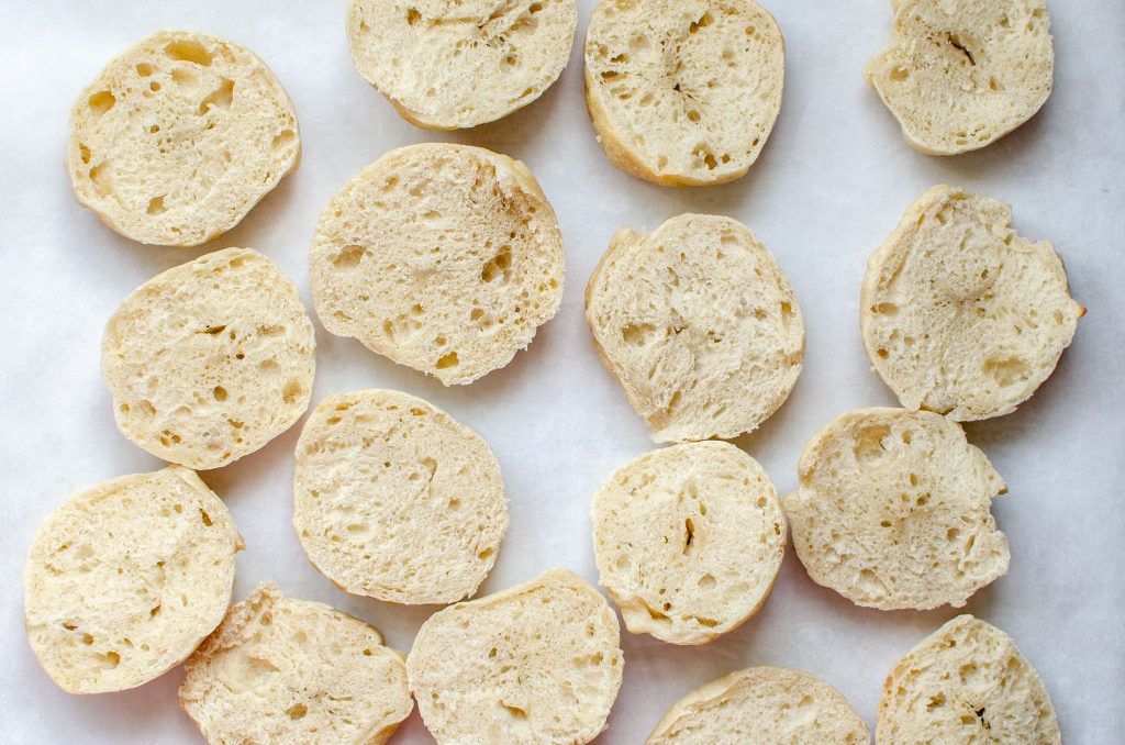 mini sourdough plain bagels cut in halves on parchment paper with cut side up