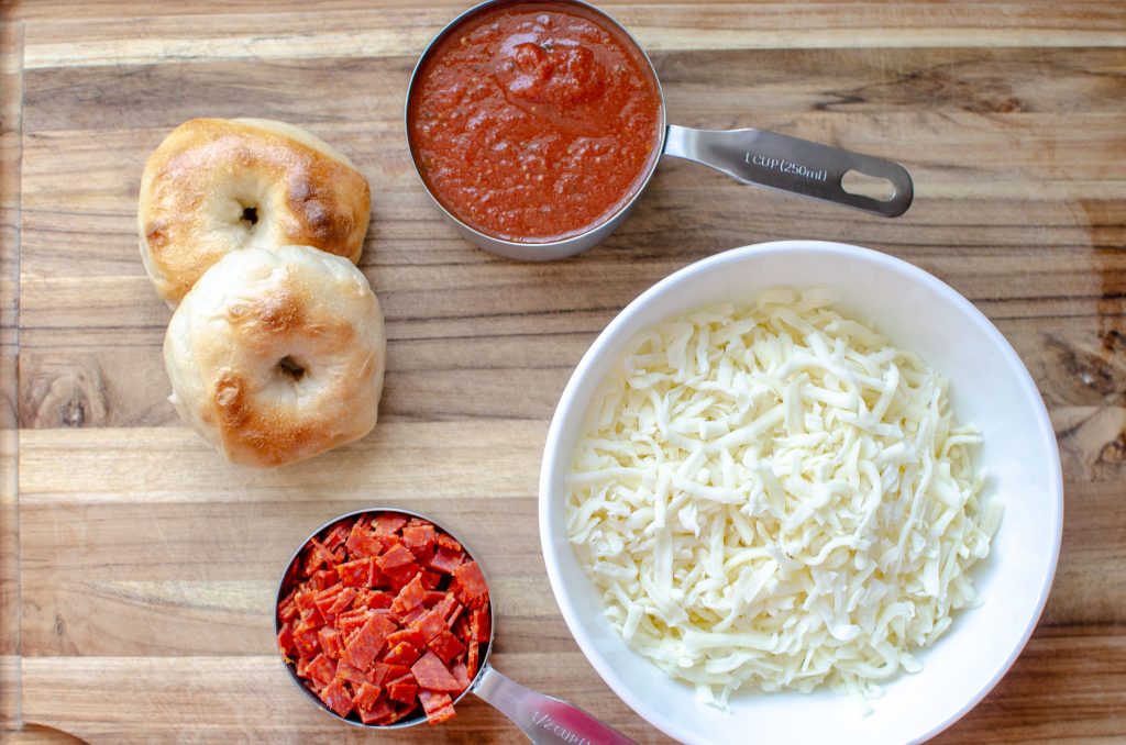 A bowl of shredded mozzarella, pizza sauce, 2 mini bagels, and diced pepperoni 