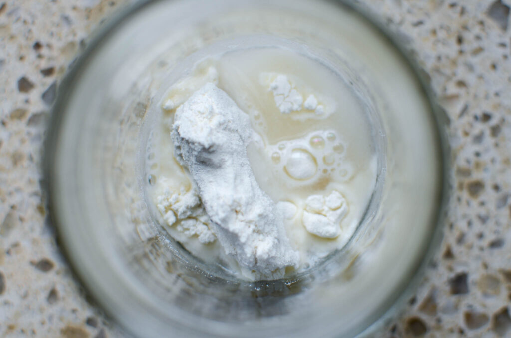 Glass jar with frozen discard, fresh flour, and warm water