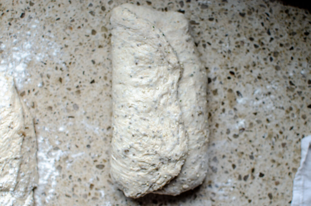 Folding the left side of the seeded multigrain sourdough bread dough over to the middle