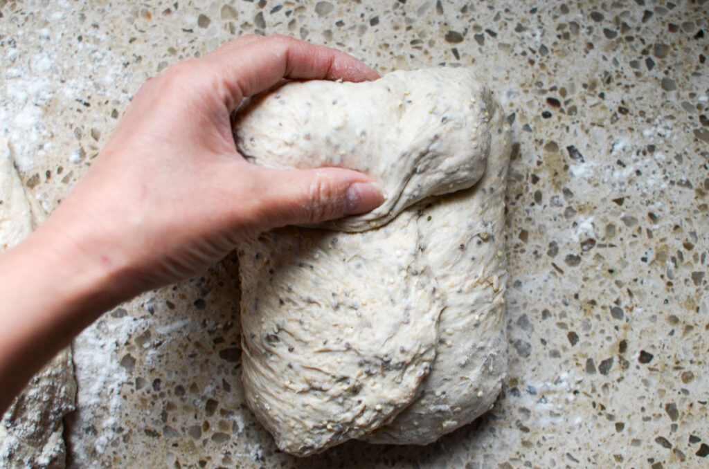 rolling the top of the seeded multigrain sourdough bread dough down through  to the middle