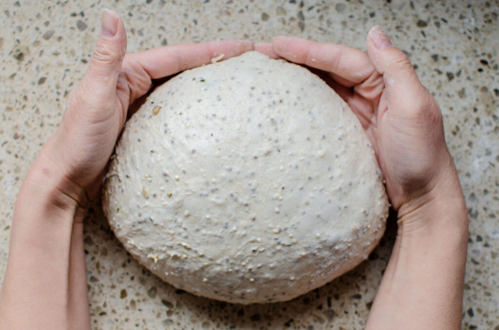 Using two hands to shape the seeded multigrain sourdough bread dough in a ball