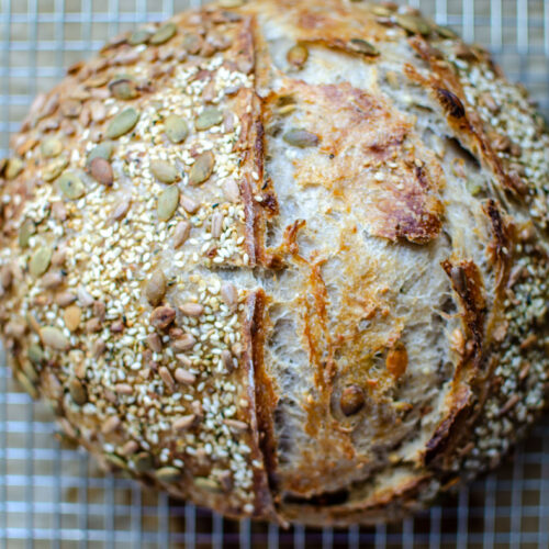 Seeded multigrain sourdough bread loaf on a wire cooling rack